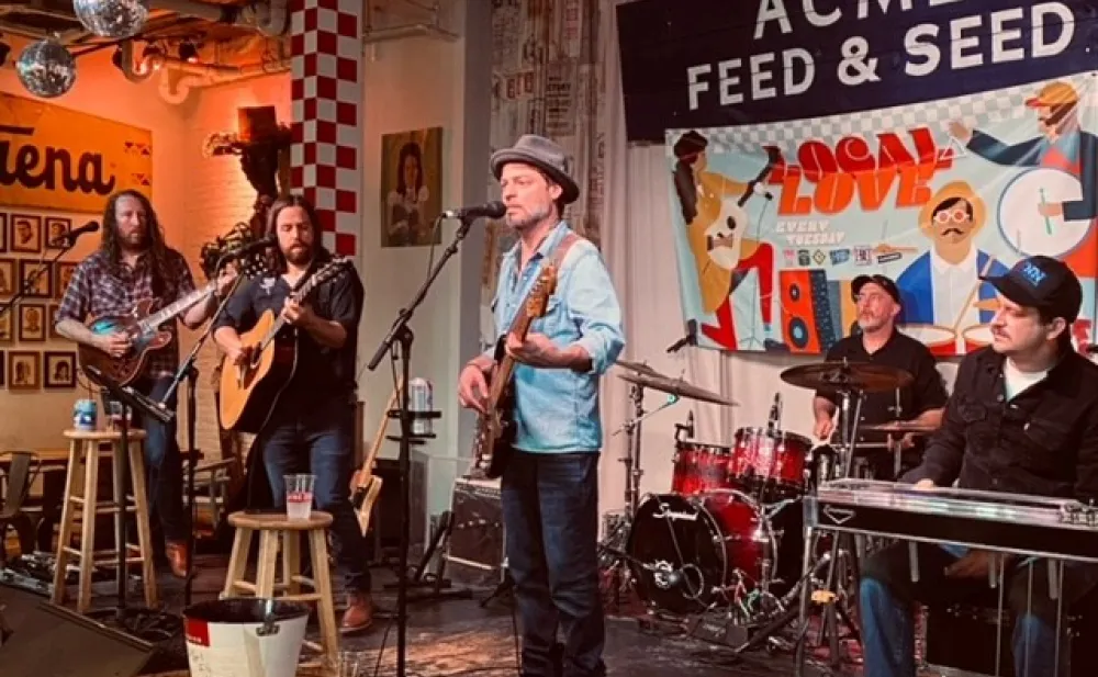 Photo: five men play in a band on stage with ACME FEED & SEED on a sign in the background.